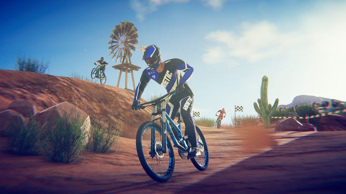 A mountain biker pedals downhill as two competitors come over the horizon behind him.