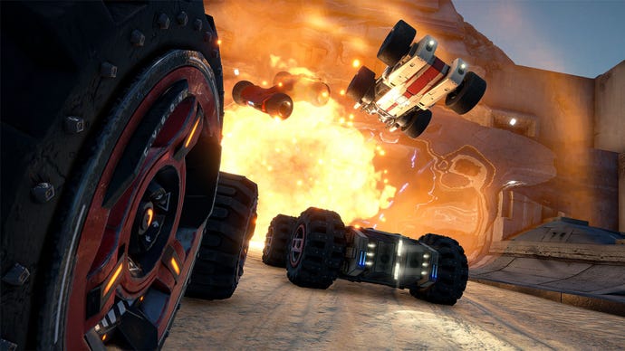 Four futuristic cars with chunky wheels drive into the flames of an explosion.